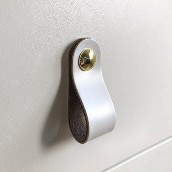 De Tomasso White handgreep van yessential.nl, met bruine randen en een gouden sluiting, brengt verfijnde elegantie op elk glad wit oppervlak.