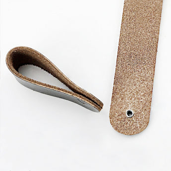 Twee stukken bruin leer - een platte strook met een zeilring en een strook met een lus - rusten op een witte achtergrond, ideaal als lederen handgrepen voor je Tomasso White kast van yessential.nl.