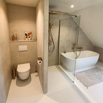 Moderne badkamer met wandcloset, gouden armaturen, glazen inloopdouche en vrijstaand bad. De Branco Gold toiletborstelhouder van yessential.nl zit bij het toilet en past naadloos bij de minimalistische inrichting erboven.