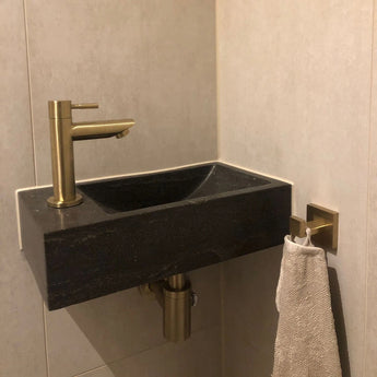 Een lichtgekleurd handdoek hangt aan de geborsteld goud Verano Gold WC set van yessential.nl, wat subtiele elegantie toevoegt aan deze goudkleurige toiletaccessoires.