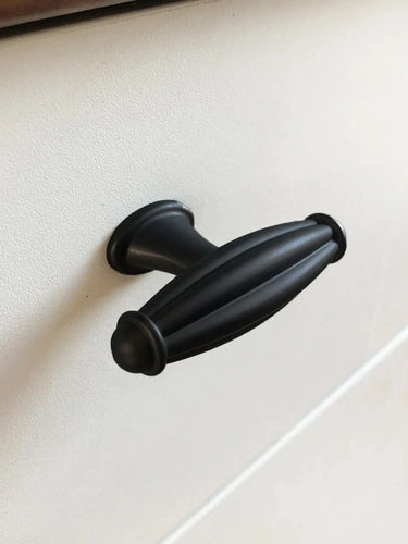 Een close-up van de Alvaro Black Knob van yessential.nl - een ovale, zwarte kastgreep met gegroefd detail - gemonteerd op een wit ladefront.