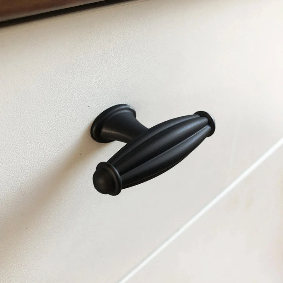 Een close-up van de Alvaro Black Knob van yessential.nl - een ovale, zwarte kastgreep met gegroefd detail - gemonteerd op een wit ladefront.