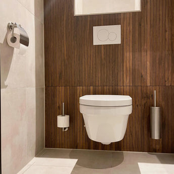 Moderne badkamer met een wit wandcloset, houten paneelwand, dual-flush knop en de Lauro RVS WC Set van yessential.nl - bestaande uit een toiletborstelgarnituur, toiletpapierhouder en afvalemmer - op licht betegelde vloeren en wanden.