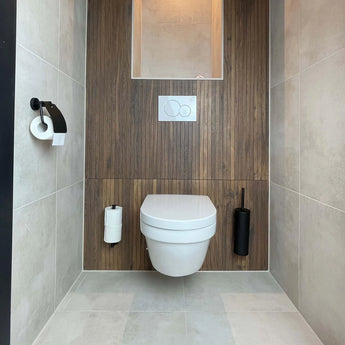 Een moderne badkamer heeft een wandcloset met houten lambrisering, lichtgrijze tegels en de Mano Black WC-set van yessential.nl - een matzwarte toiletborstel en papierhouder - plus een witte spoelplaat erboven.