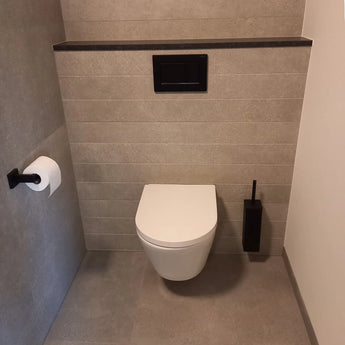 Een moderne badkamer met een wandcloset, grijze tegels, een zwarte spoelknop, de yessential.nl Alessino Black matzwarte toiletborstel met houder en een toiletpapierhouder aan de linkermuur.