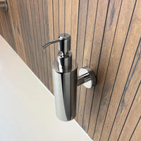 Het Alberto Chrome zeeppompje van yessential.nl is stijlvol en wordt muurbevestigd op een verticale houten wand boven een wit aanrecht.