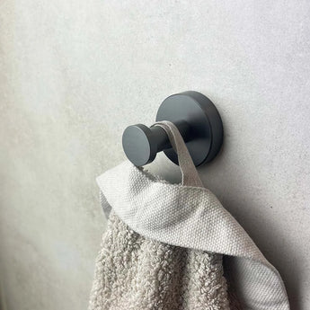 Een close-up van een grijze handdoek op een rond, gunmetal wandhaakje uit de yessential.nl Midao Gunmetal WC-set - een geraffineerd detail voor elke moderne badkamer of luxe WC-accessoires verzameling.