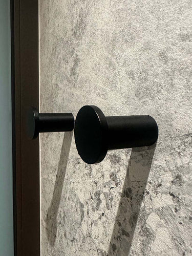 Vier zwarte cilindrische Carreno handdoekhaakjes van yessential.nl, gemaakt van roestvrij staal, zijn gemonteerd op een gestructureerde wand van grijze steen - een elegante en moderne badkameraccessoire.