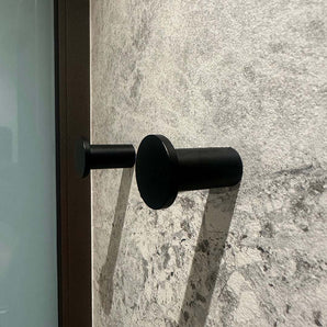 Vier zwarte cilindrische Carreno handdoekhaakjes van yessential.nl, gemaakt van roestvrij staal, zijn gemonteerd op een gestructureerde wand van grijze steen - een elegante en moderne badkameraccessoire.