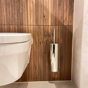 Een modern wandcloset is gecombineerd met de Pacho Chroom WC set van yessential.nl, met een glanzend zilveren borstelhouder, en dat alles tegen een verticale houten lambrisering en lichte tegelvloer.