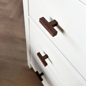 Een close-up van een wit dressoir met de Vigio Walnut Knob van yessential.nl op een lichte houten vloer, waarbij het contrast tussen de donkere walnoten knop en de strakke witte ladefronten goed naar voren komt.