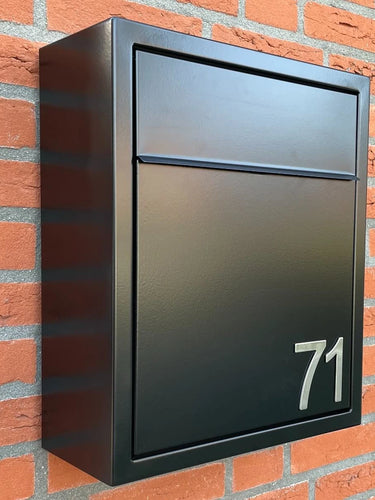 Een zwarte metalen brievenbus met het nummer 71, met Animo RVS 5cm (geen boor) nummers van yessential.nl, is gemonteerd op een rode bakstenen muur.