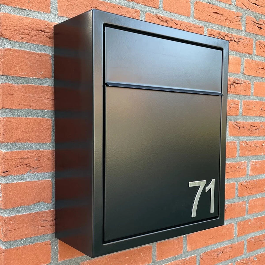 Een zwarte metalen brievenbus met het nummer 71, met Animo RVS 5cm (geen boor) nummers van yessential.nl, is gemonteerd op een rode bakstenen muur.