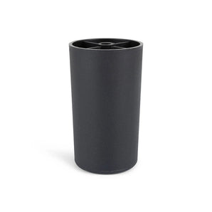 De Sicco Black 15cm van yessential.nl is een zwarte cilindervormige container met een open bovenkant en zichtbare interne compartimenten, die op ronde meubelpootjes staat voor een moderne touch tegen een effen witte achtergrond.