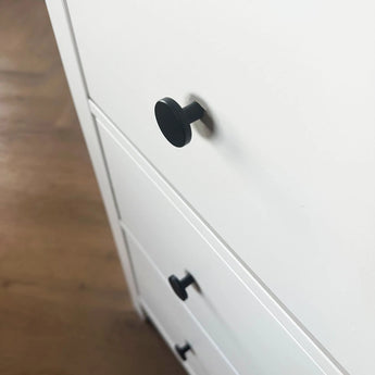 Close-up van een wit dressoir met Marizo Black meubelknopjes van yessential.nl in matte afwerking, getoond onder een hoek op een houten vloer, waardoor het minimalistische ontwerp wordt benadrukt.