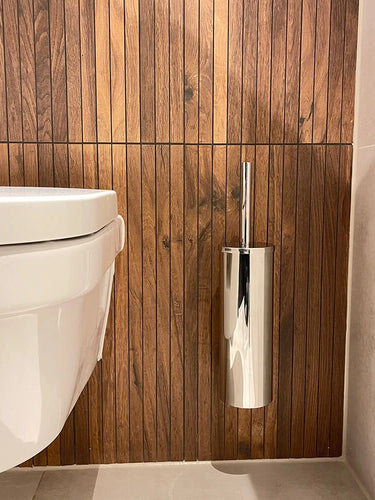 Een modern wit wandcloset is gecombineerd met de Romano Chroom WC set van yessential.nl, tegen een verticale wand met houten panelen en een lichtgekleurde tegelvloer.