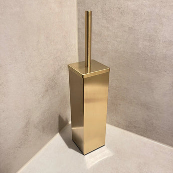 De Velasco Gold toiletborstel van yessential.nl, vrijstaand met houder, staat in de hoek van een badkamer met beige betegelde muren en vloer.