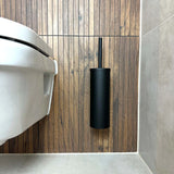 Een moderne badkamer is voorzien van een wandcloset en de Branco Black toiletborstelhouder met zwart borstel van yessential.nl, beide bevestigd aan een houten wand naast lichtgrijze betegelde oppervlakken.